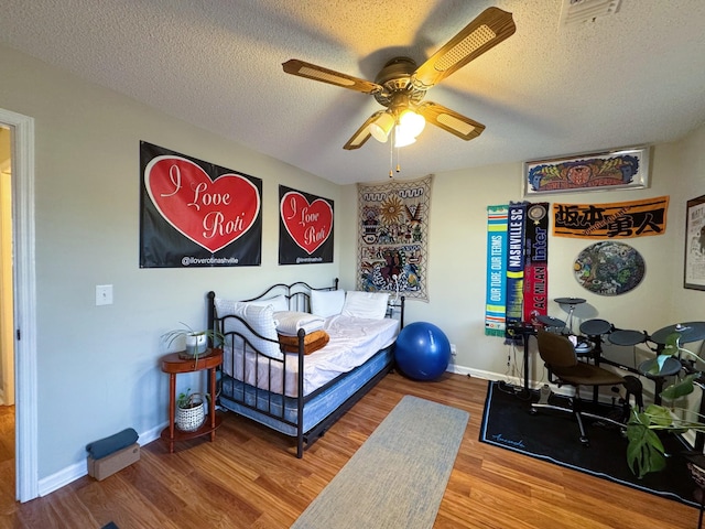 bedroom featuring ceiling fan, a textured ceiling, baseboards, and wood finished floors