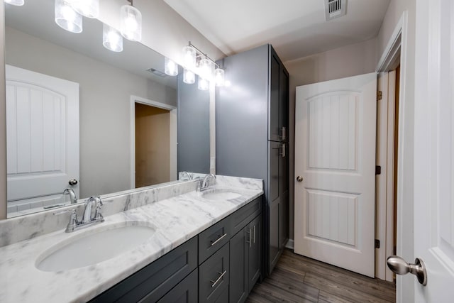 bathroom with double vanity, visible vents, a sink, and wood finished floors