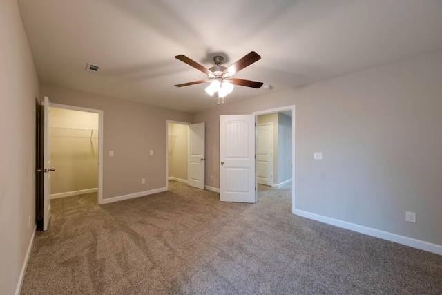 unfurnished bedroom with visible vents, a ceiling fan, baseboards, carpet, and a walk in closet