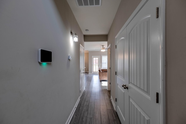 hall with dark wood-type flooring, visible vents, and baseboards