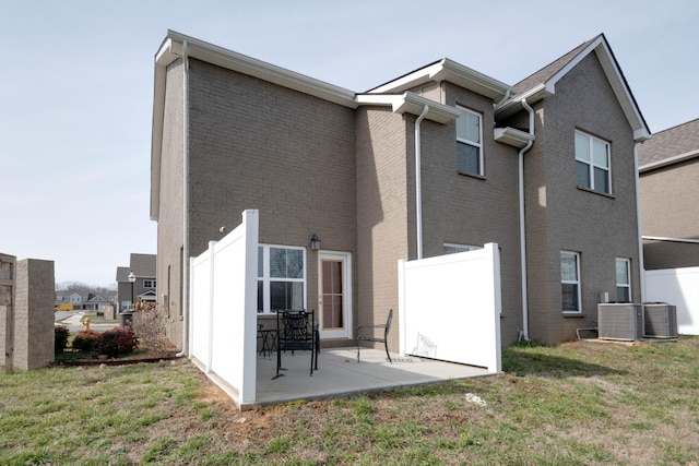 rear view of property with brick siding, a yard, a patio, central AC, and fence