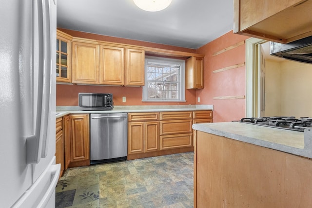 kitchen featuring glass insert cabinets, stone finish floor, stainless steel appliances, and light countertops