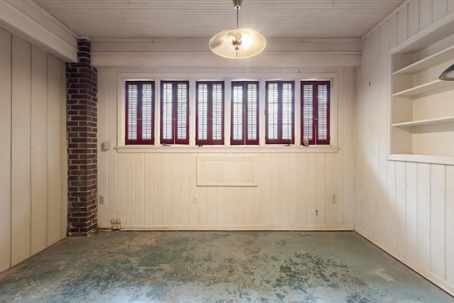 unfurnished room with wood walls, built in shelves, and concrete flooring