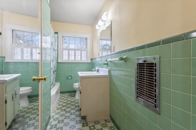 full bathroom featuring heating unit, vanity, toilet, and tile walls