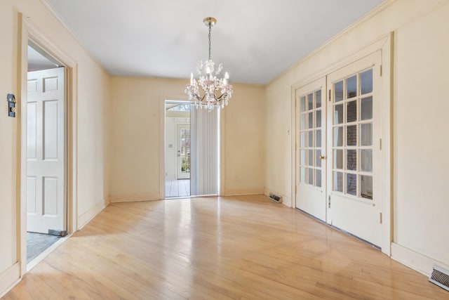 unfurnished dining area with a chandelier, baseboards, visible vents, and light wood finished floors