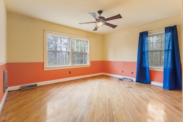 spare room with a ceiling fan, wood-type flooring, visible vents, and baseboards