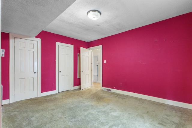 unfurnished bedroom featuring a textured ceiling, carpet flooring, visible vents, and baseboards