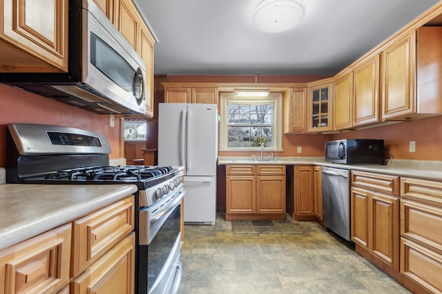 kitchen with glass insert cabinets, appliances with stainless steel finishes, stone finish flooring, light countertops, and a sink