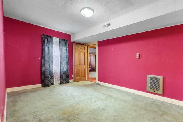 carpeted empty room featuring a textured ceiling, heating unit, visible vents, and baseboards