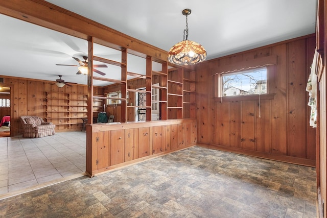 interior space featuring built in shelves, stone finish flooring, wooden walls, and a ceiling fan