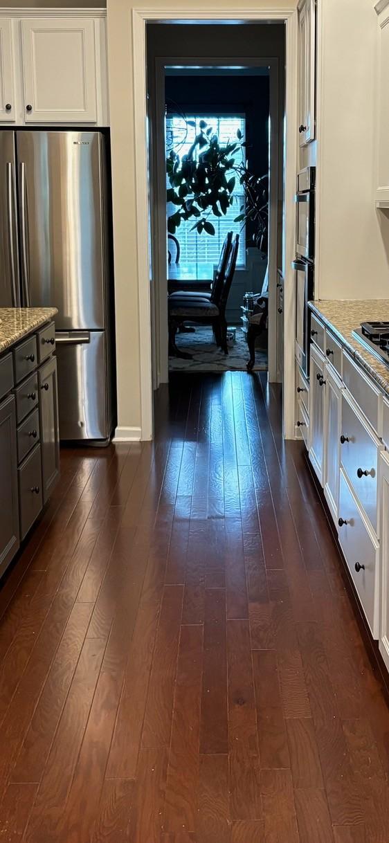 kitchen with white cabinets, dark wood-style flooring, freestanding refrigerator, and light stone countertops