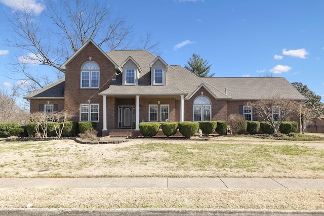 view of front of house featuring a shingled roof, a front yard, and brick siding