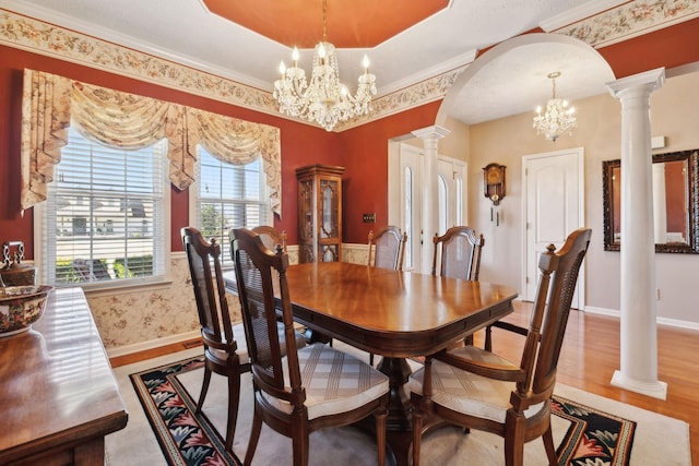 dining space featuring arched walkways, wood finished floors, a chandelier, and decorative columns