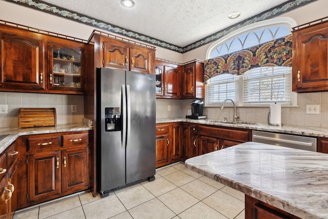 kitchen featuring light tile patterned floors, glass insert cabinets, appliances with stainless steel finishes, light stone counters, and a sink