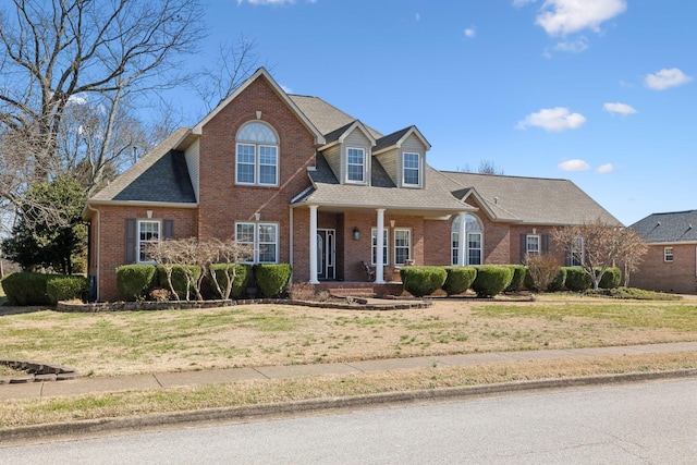 view of front of house featuring roof with shingles, brick siding, a porch, and a front yard