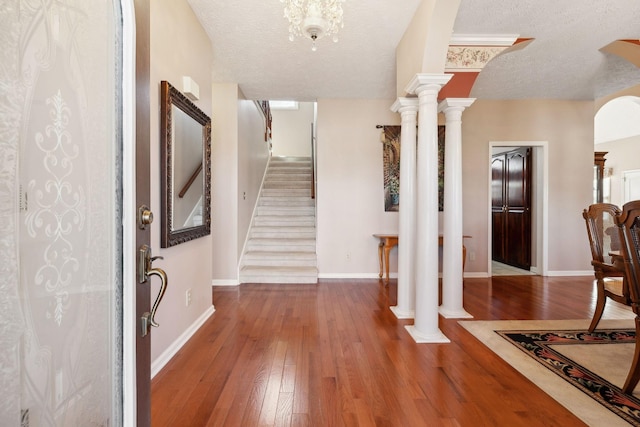 foyer with ornate columns, a textured ceiling, arched walkways, and hardwood / wood-style floors