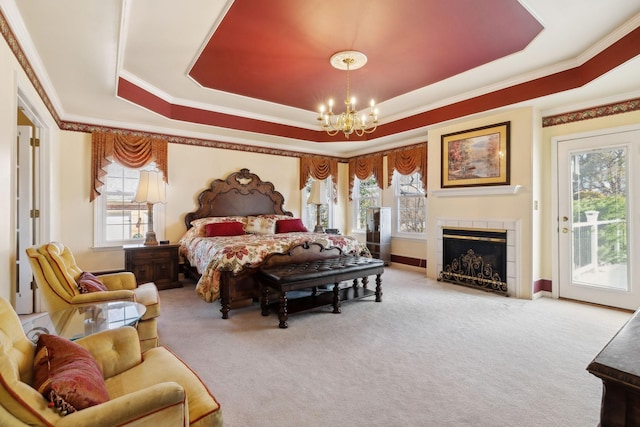 carpeted bedroom featuring access to exterior, crown molding, a notable chandelier, a raised ceiling, and a tile fireplace