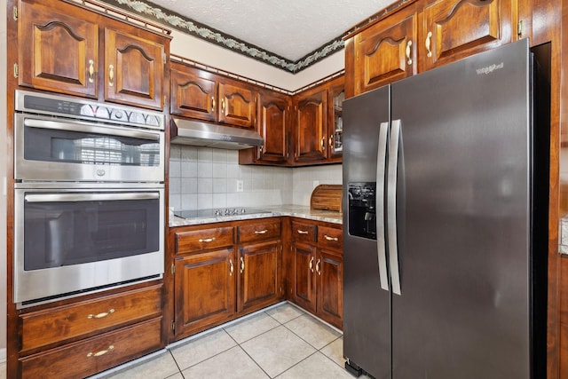 kitchen with light tile patterned floors, tasteful backsplash, appliances with stainless steel finishes, a textured ceiling, and under cabinet range hood