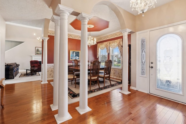 foyer featuring a notable chandelier, a textured ceiling, wood-type flooring, and ornate columns