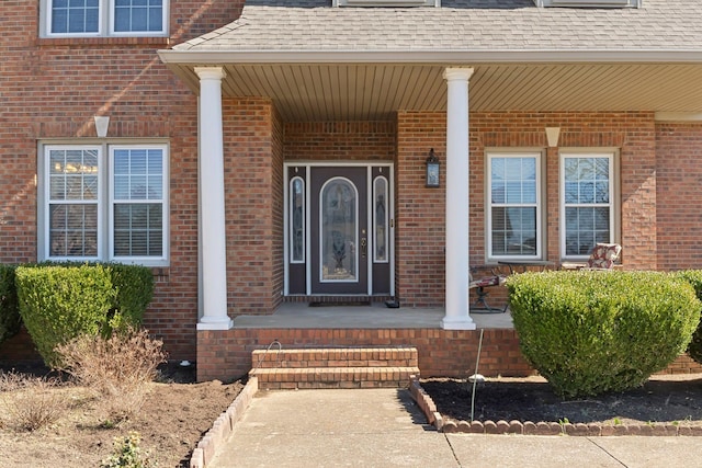 entrance to property with covered porch, roof with shingles, and brick siding