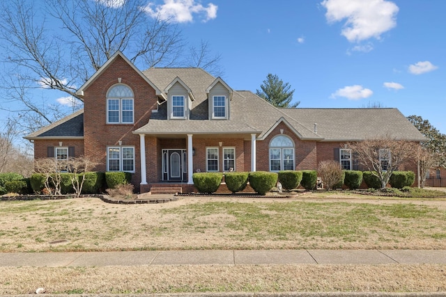 view of front of home featuring brick siding, a front lawn, and a shingled roof