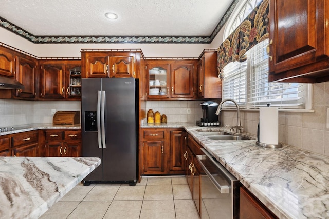 kitchen with light tile patterned floors, appliances with stainless steel finishes, glass insert cabinets, a sink, and light stone countertops