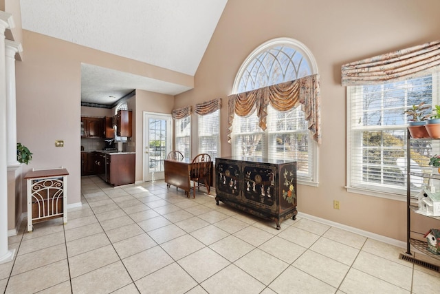 interior space featuring decorative columns, light tile patterned flooring, a textured ceiling, high vaulted ceiling, and baseboards