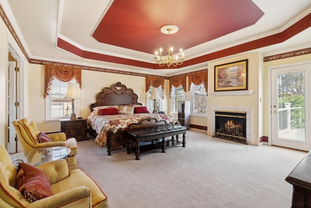 carpeted bedroom with a fireplace, access to exterior, ornamental molding, a tray ceiling, and an inviting chandelier