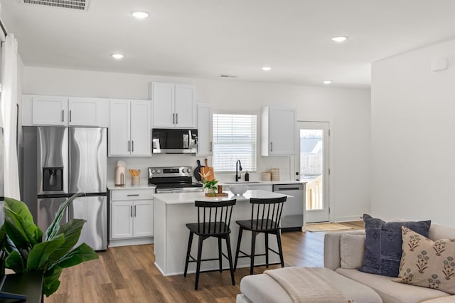 kitchen with a kitchen island, stainless steel appliances, a kitchen bar, white cabinetry, and a sink