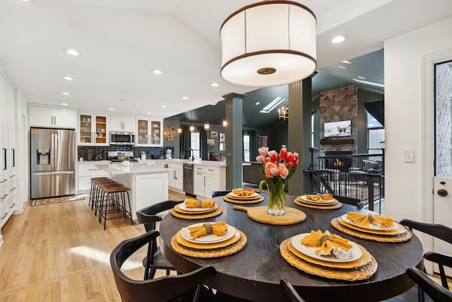 dining space with recessed lighting, a large fireplace, vaulted ceiling, and light wood-style flooring