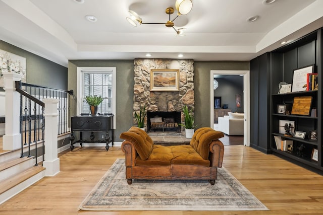 living room featuring light wood-style floors, a fireplace, stairway, and a raised ceiling