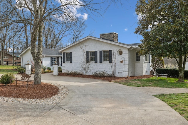 single story home featuring brick siding, concrete driveway, a chimney, crawl space, and a front yard