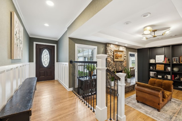 foyer with light wood-type flooring, a wainscoted wall, a fireplace, and crown molding