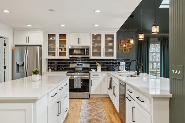 kitchen with tasteful backsplash, light wood-style flooring, a peninsula, stainless steel appliances, and a sink