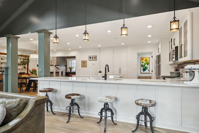 kitchen featuring a breakfast bar, stainless steel appliances, light wood-style floors, a sink, and ornate columns