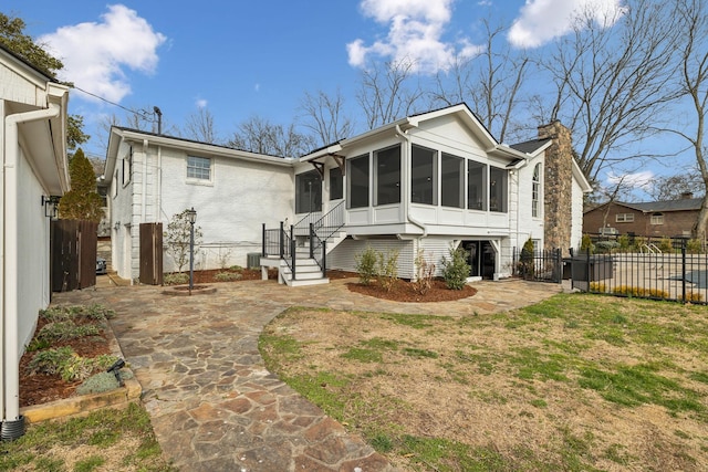 view of front of home featuring a sunroom, brick siding, fence, and a chimney