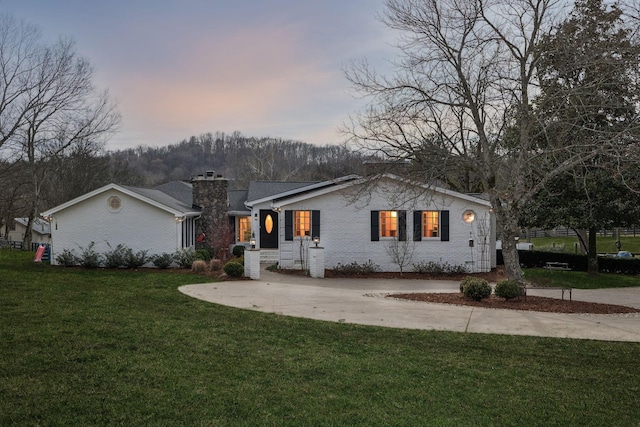 view of front of house featuring concrete driveway, brick siding, a chimney, and a front lawn