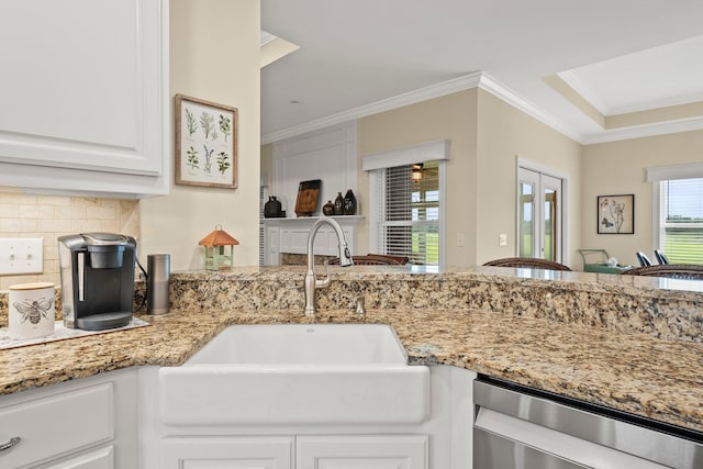 kitchen with light stone counters, decorative backsplash, ornamental molding, a sink, and dishwasher