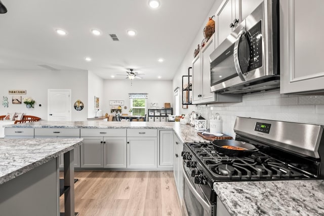 kitchen with visible vents, decorative backsplash, appliances with stainless steel finishes, light wood-style floors, and a peninsula