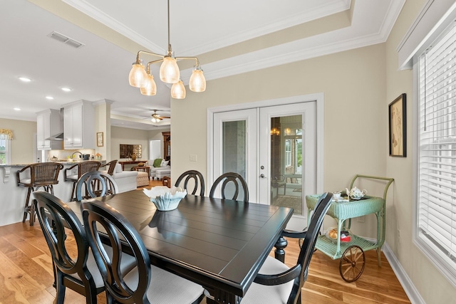 dining space with french doors, crown molding, light wood finished floors, visible vents, and ceiling fan with notable chandelier