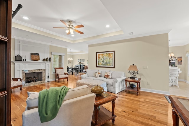 living room with ornamental molding, light wood-type flooring, a raised ceiling, and a fireplace