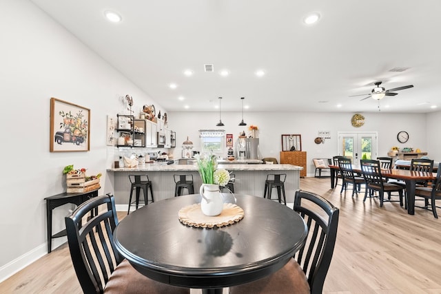 dining space with baseboards, indoor bar, french doors, light wood-type flooring, and recessed lighting