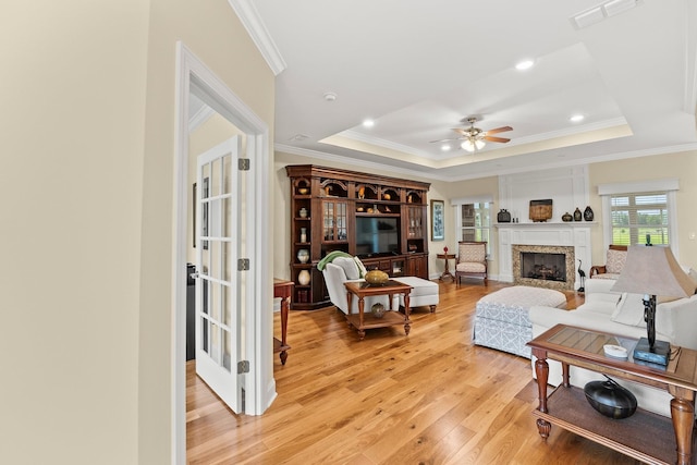 living room with visible vents, light wood-style flooring, a tray ceiling, crown molding, and a high end fireplace