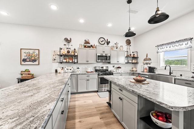 kitchen featuring open shelves, appliances with stainless steel finishes, light wood-type flooring, and a sink