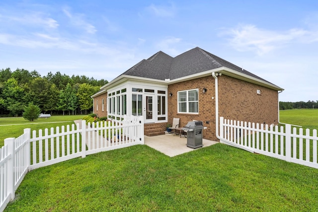 back of house featuring a sunroom, brick siding, a patio, and a lawn