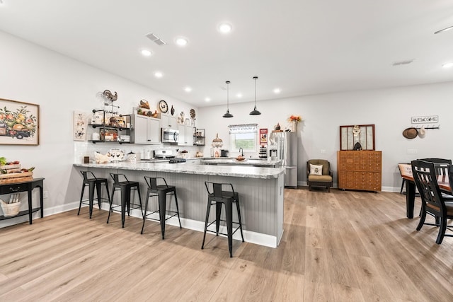 kitchen featuring a peninsula, open shelves, appliances with stainless steel finishes, and a breakfast bar