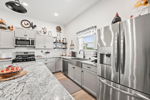 kitchen featuring stainless steel appliances, decorative backsplash, light wood-style floors, a sink, and light stone countertops