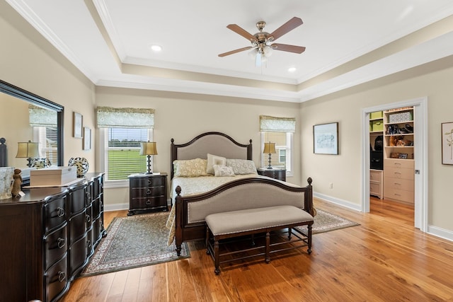 bedroom with light wood finished floors, ornamental molding, and a raised ceiling