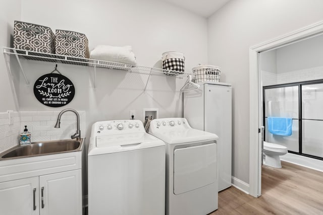 washroom with light wood-style floors, independent washer and dryer, cabinet space, and a sink