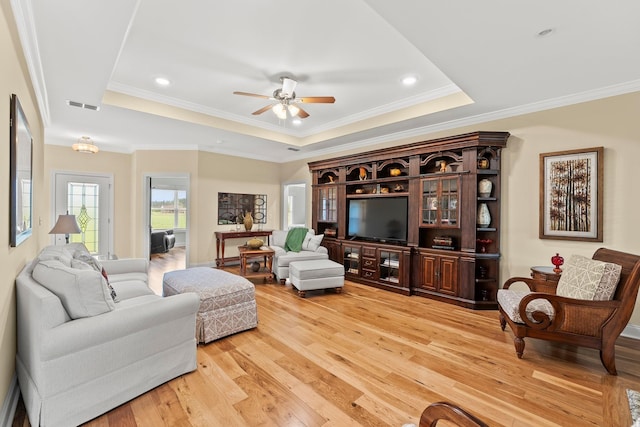 living area featuring light wood-style floors, visible vents, a tray ceiling, and crown molding